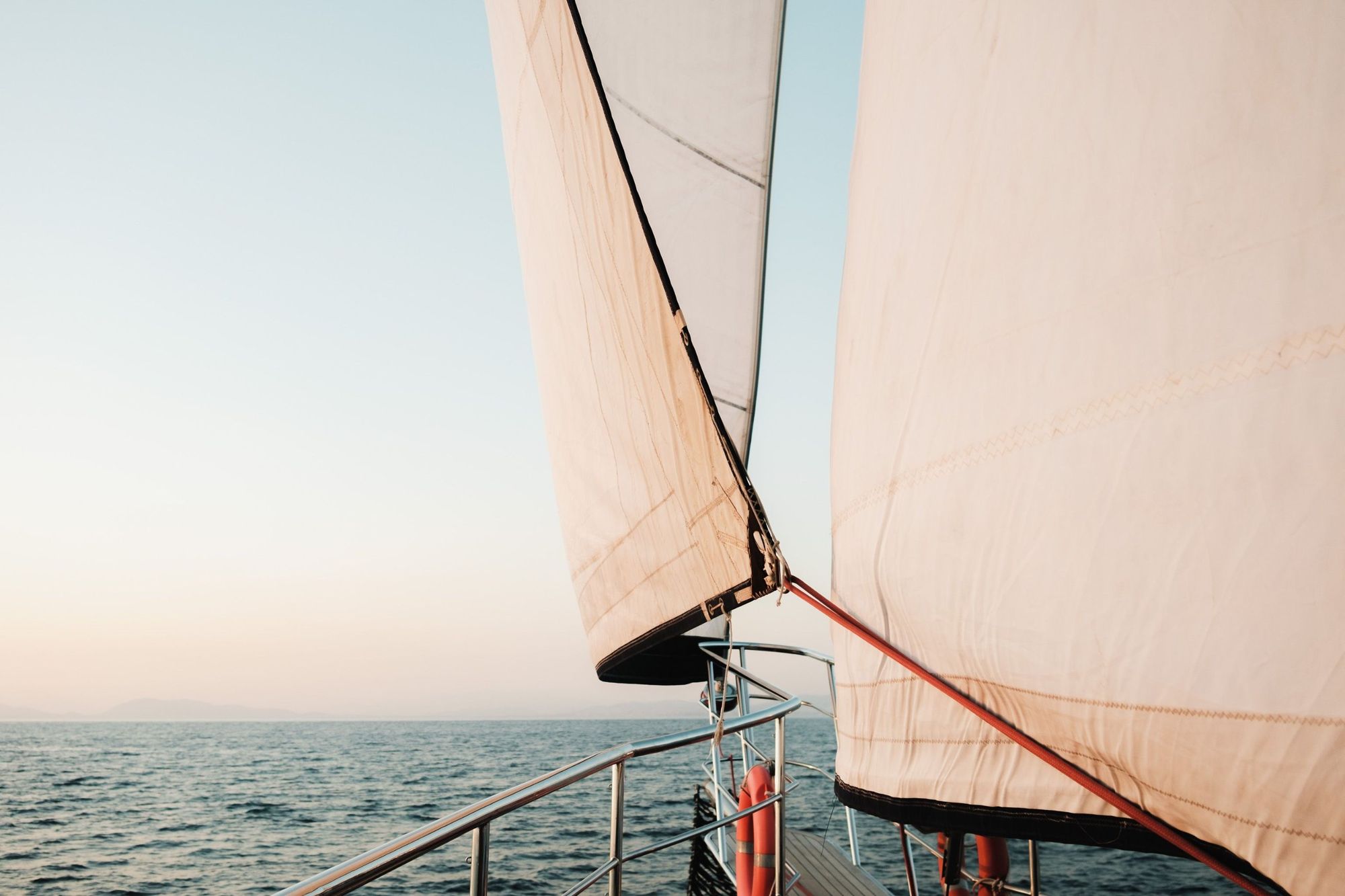 Looking forward from the bow of a sailboat under full sail at dusk